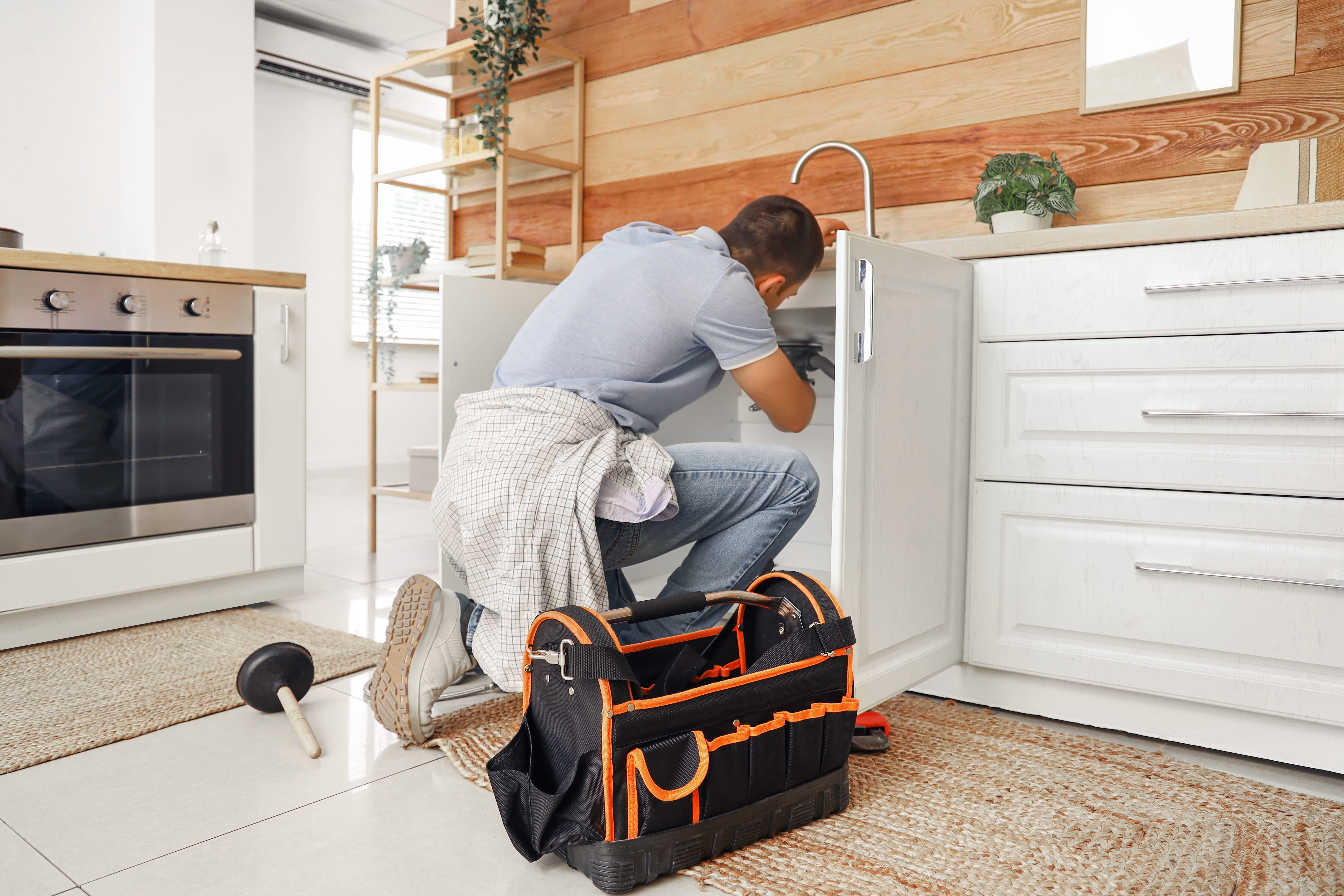 Male plumber fixing sink in kitchen, back view